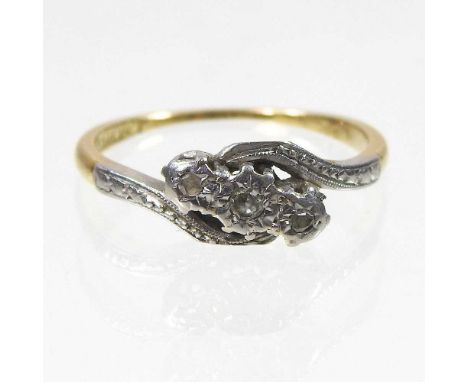 An 18 carat gold and platinum set three stone diamond ring, of crossover design, with textured shoulders, 2.0g, size L