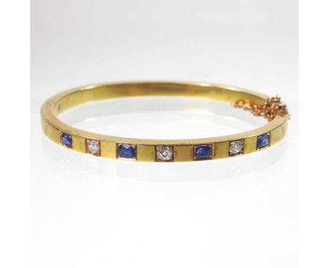 An early 20th century 18 carat gold sapphire and diamond bangle, of hinged design, set with a row of seven alternating stones