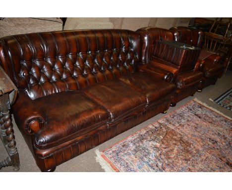 A red stained leather drawing room suite, to include; a three-seater settee and two wing armchairs with button backs; togethe