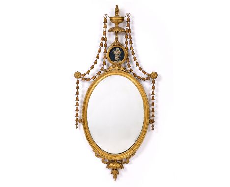 AN ADAM STYLE GILTWOOD OVAL HANGING WALL MIRROR with urn finial hung with bell flowers and with inset painted putti, 110cm x 