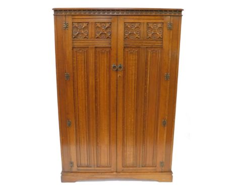 An Elizabethan style oak double wardrobe, with foliate and linen fold carved panelled doors, raised on a plinth bracket base,