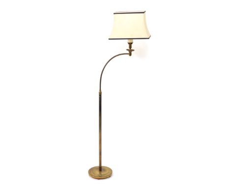A brass standard lamp, with a curved arm, raised on a loaded circular base, with shade, 150cm high.