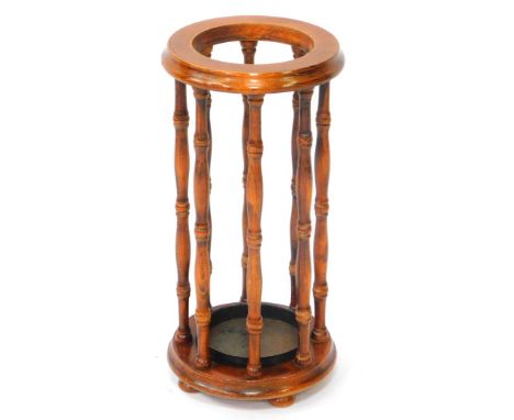 An oak circular umbrella and stick stand , with metal drip tray and spindle frame, raised on a circle base over three bun fee