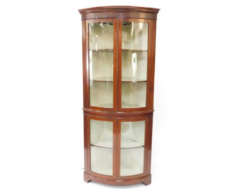 An Edwardian mahogany bowfront corner display cabinet, the outswept pediment with dentil moulding above a blind fretwork frie