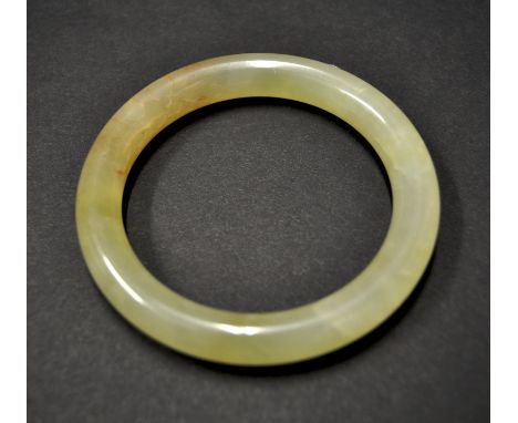 A Chinese jade bangle of mottled pale yellow-green colour with cloudy and rust red inclusions, diameter 7.8cm