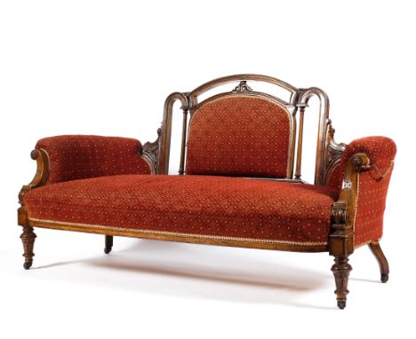 A Victorian walnut framed upholstered sofa, with arched pierced back carved with scrolls and flanked by columns, upholstered 