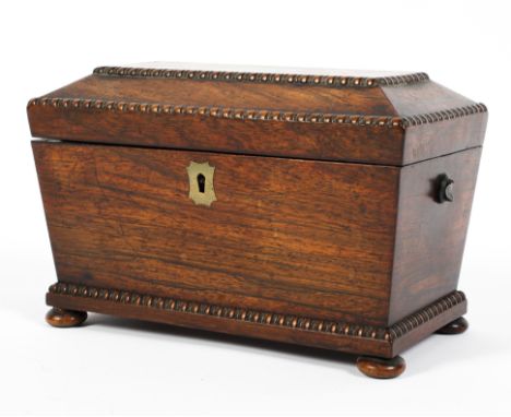 An early 19th century rosewood tea caddy, of sarcophagus form, with gadrooned edges and a brass escutcheon, raised on bun fee