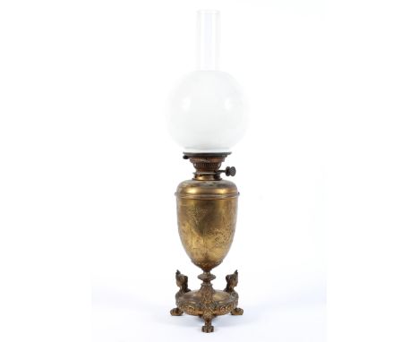 A late 19th century brass oil lamp, the urn shaped body with embossed foliate decoration, raised upon unusual tripod lion paw