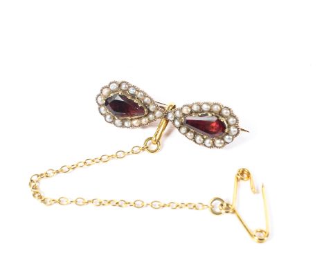 A 19th century 9ct gold garnet and seed pearl bow brooch set with two pear cut foil backed garnets with a surround of split s