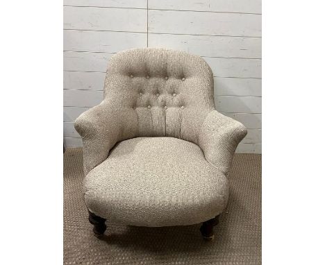 An upholstered tub arm chair with button back on mahogany legs and ceramic castors  