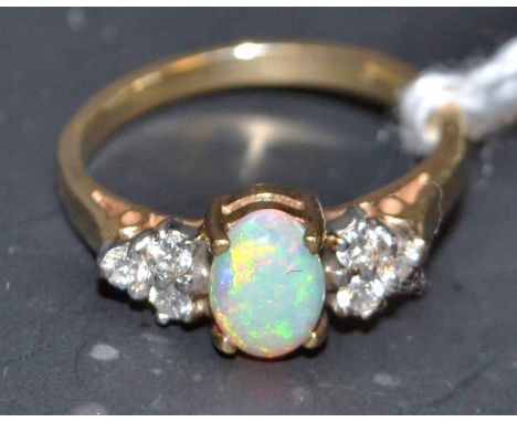 An opal and diamond cluster ring, central oval opal, flashing green, red and blue colour play, flanked to each side by a tria