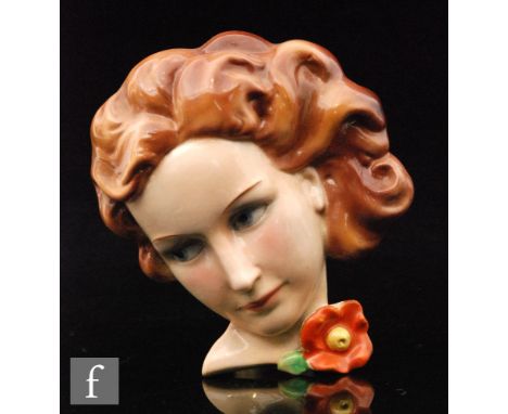 A 1930s Goebel wall mask modelled as a female with side glancing blue eyes, brown hair and a deep orange flower, impressed cr