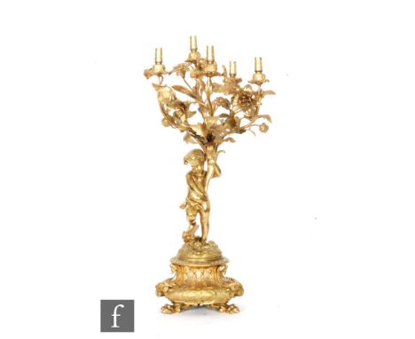 A gilt metal five-light lamp, detailed with a floral spray held aloft in a cornucopia by a cherub stood on a flaming torch, a