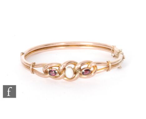 An early 20th Century 9ct rose gold hinged bangle set with garnets flanking a central cabochon cut opal, total weight 10g, S/