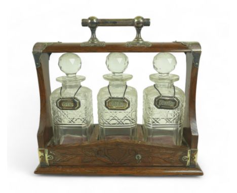 A Victorian oak tantalus, with EPNS mounts and carved decoration, containing three clear glass part hobnail cut decanters and