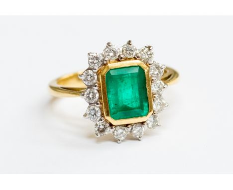 An emerald and diamond 18ct white gold cluster ring, comprising an oval rub over set emerald to the centre approx 6 x 9mm, wi