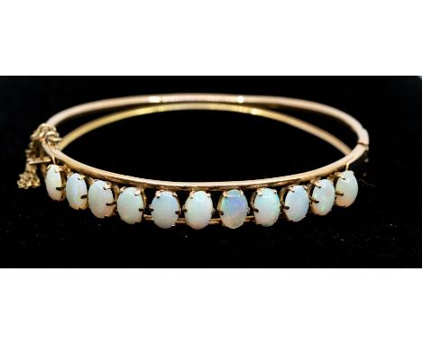 An opal and 14ct rose gold bangle, comprising a row of eleven claw set oval opals, each approx 7 x 4mm, within round wire bor