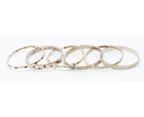 A collection of silver bangles to include two set with garnet stones, two bark effect textured versions, one with twist decor