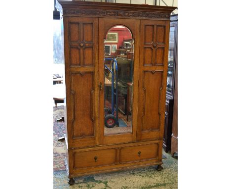 An early 20th century oak wardrobe, stepped cornice, central arched panel door flanked by panels, deep drawer to base, turned