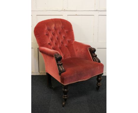 A Victorian mahogany framed button back armchair, with scroll carved arms, on turned front legs and castors