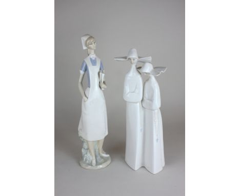 A Lladro porcelain figure of a nurse holding books, hand in pocket, 36cm high, and another of two nuns (a/f - hat chipped)