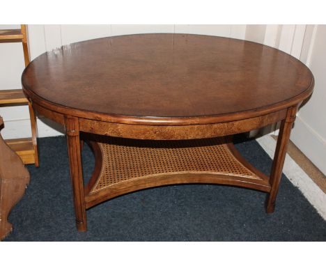 A modern oval burr wood coffee table with cane under-shelf, 107cm