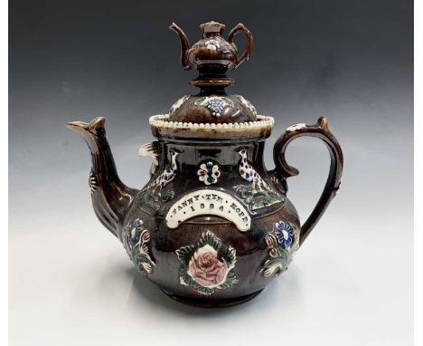 A Victorian Measham treacle glazed bargeware teapot, dated 1884, with teapot finial, applied with pheasants and flowerheads, 