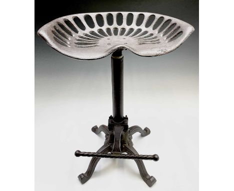 A cast iron tractor seat style stool, with plain column support, raised on four feet and with a footrest. Height 64cm.