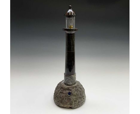 A substantial Cornish serpentine table lamp, modelled as a lighthouse, on a naturalistic rocky base mounted with an enamel pl