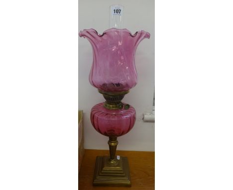 A oil lamp with cranberry glass reservoir and shade on brass stepped base, overall height to top of shade 50cm.