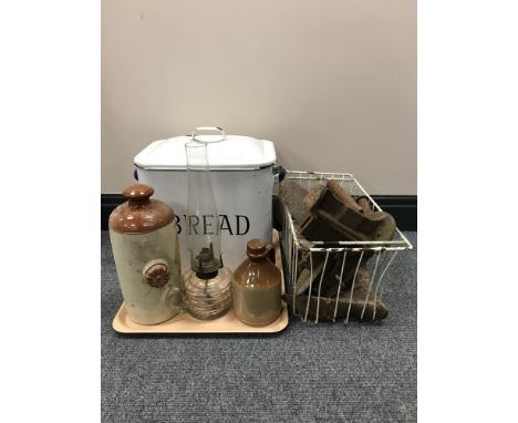 A tray of enamelled bread bin, two stone ware bottles, glass oil lamp and a basket of cobbler's lasts and flat irons 
