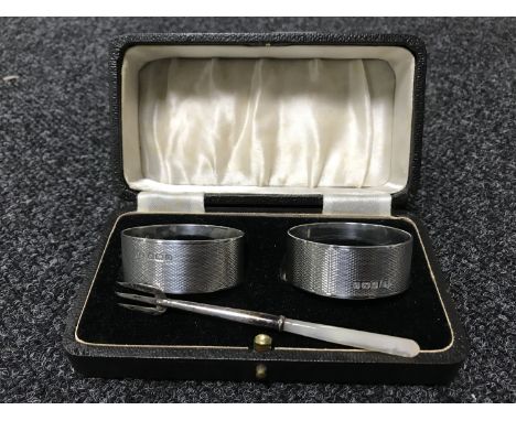 A pair of cased silver napkin rings together with a silver pickle fork