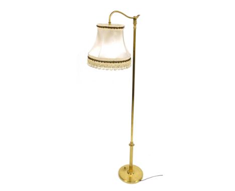 A 20thC brass standard lamp, with a shaped arm, supporting a fabric shade, raised on a partially fluted column over a circula