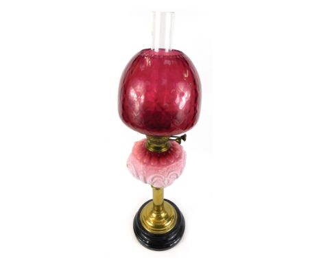 A Victorian cranberry glass oil lamp, with an opaline pink reservoir and cranberry glass shade, on brass column support above