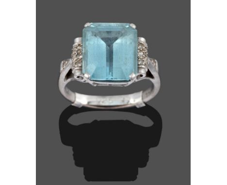 An Aquamarine and Diamond Ring, the central emerald-cut aquamarine in a white claw setting, flanked by scroll shoulders inset