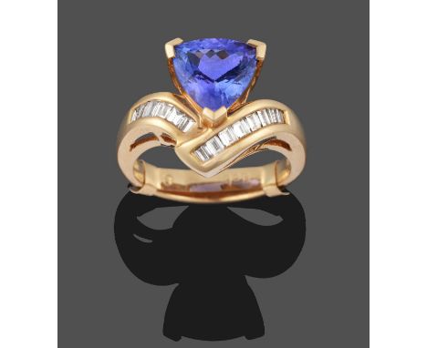 A Tanzanite and Diamond Ring, a trilliant cut tanzanite in yellow claw settings, to baguette cut diamond set asymmetric shoul