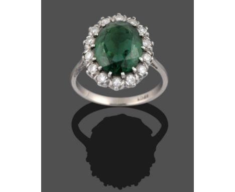 A Green Tourmaline and Diamond Cluster Ring, the oval cut green tourmaline within a border of round brilliant cut diamonds in