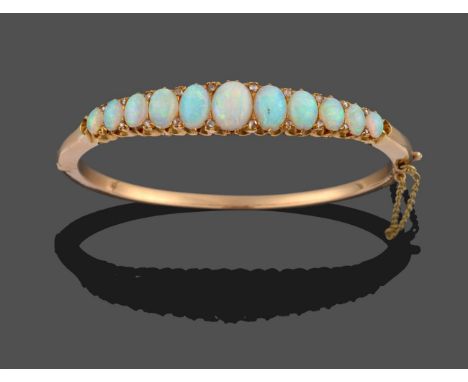 An Opal and Diamond Bangle, eleven graduated oval cabochon opals with pairs of rose cut diamond accents between, in yellow cl