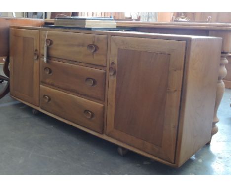 An Ercol light elm low sideboard fitted three central drawers flanked by wing cupboards.