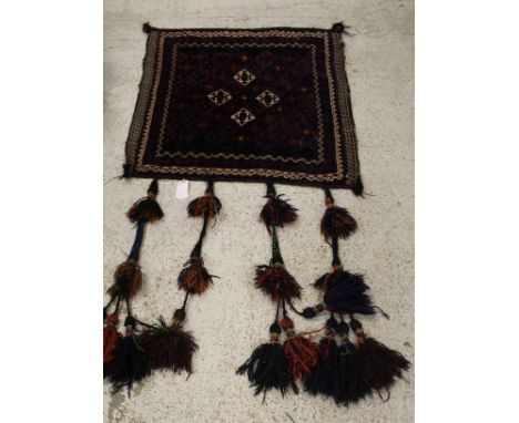 An Afghan carpet wall hanging, the repeating diamond shaped medallions in aubergine and cream on a black ground, within cream