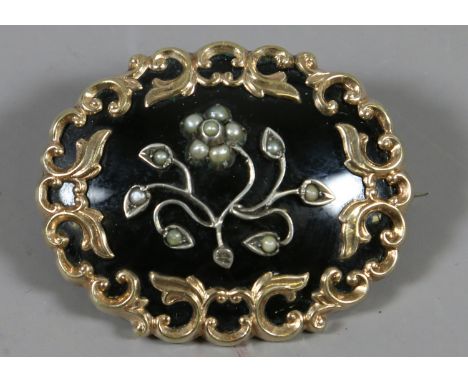 A Victorian yellow metal and black enamel mourning brooch with scroll border and a central spray studded with seed pearls. 