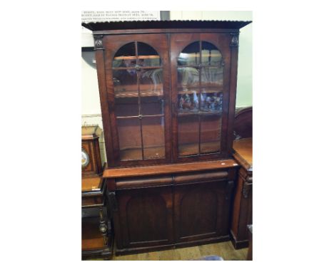 A Victorian mahogany bookcase on cupboard, having a pair of bar glazed doors above two frieze drawers, with a pair of panel d