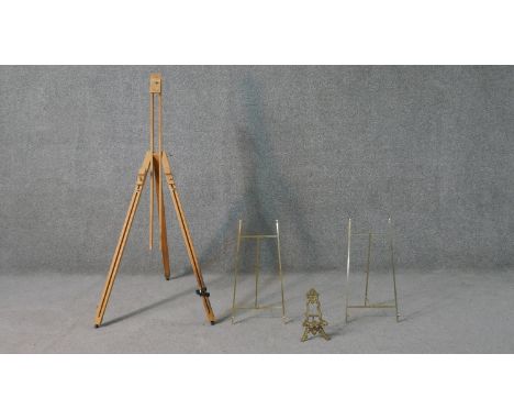 A collection of easels, including a pine artists easel, a baroque style brass easel and two other brass easels. H.140 W.150cm