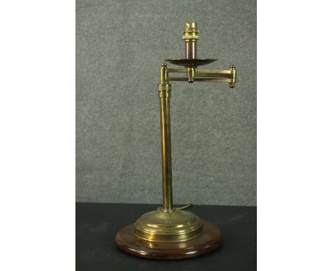 A vintage brass adjustable reading lamp, with an articulated arm and a cylindrical stem, on a circular wood base with a mould