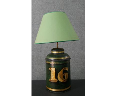 A toleware enamelled tin tea cannister, converted to a table lamp, with a green shade, the green cannister painted with the n