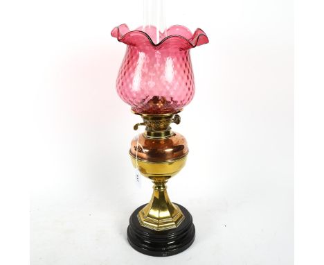 A Victorian brass and copper oil lamp on plinth, with chimney and cranberry glass shade, 59cm overall 