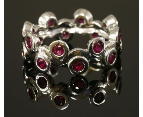 A Continential white gold, ruby band ring,with a central wavy section.  A continuous row of circular mixed cut rubies, rub se
