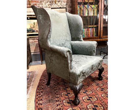 A 19th century George II style wingback armchair with grey-blue steel-stud watersilk upholstery, raised on hip carved cabriol