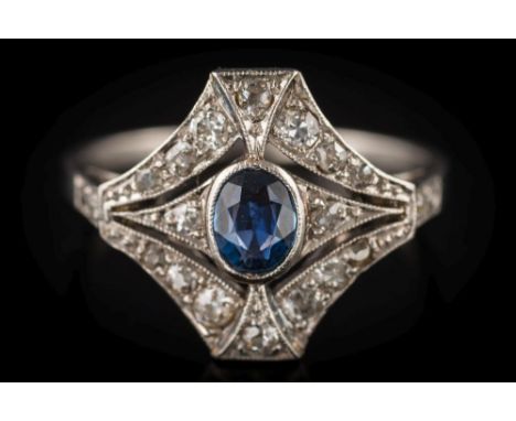 An Art Deco sapphire and diamond cluster ring: the central, oval sapphire approximately 5.5mm long x 2mm deep, within a surro