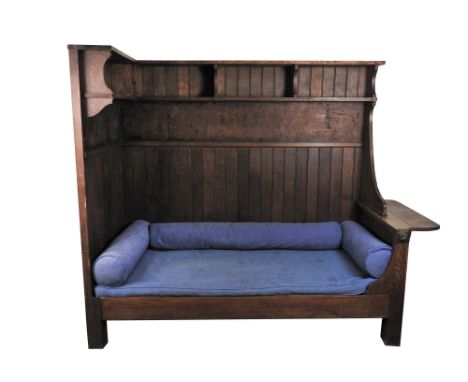 An Arts &amp; Crafts oak Bedford Park style corner day bed with tongue and groove panel back and shelves above a later uphols